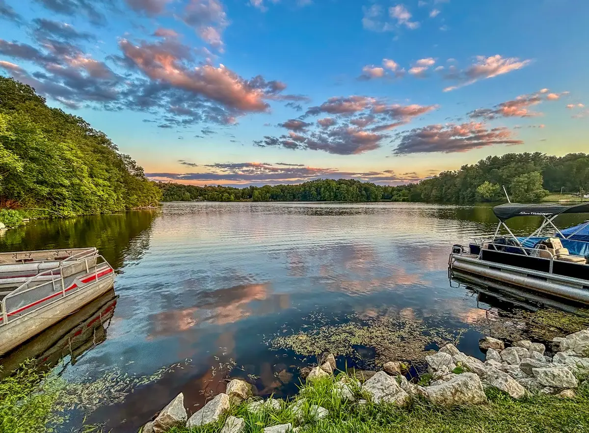 Boats docked on a peaceful lake beneath a colorful sunset